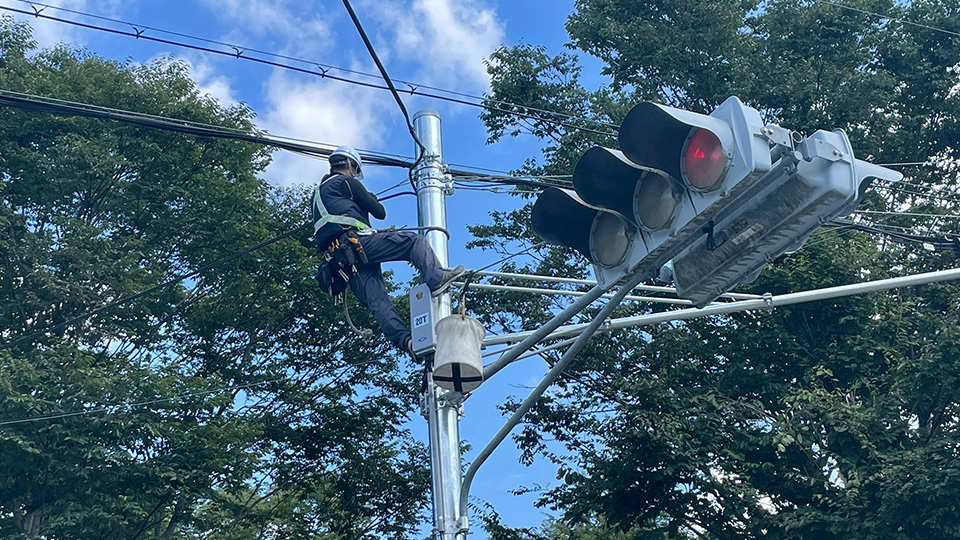 信号機のかなり高い位置まで登って配線作業を行う作業員。