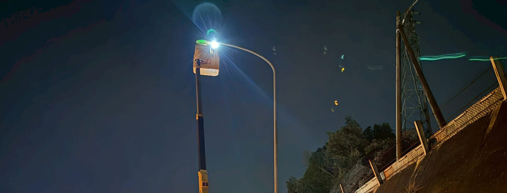 夜間の道路照明メンテナンス。高所作業車のバケットが眩しい光を放つ街路灯に接近し、暗い夜道の安全を守る作業。