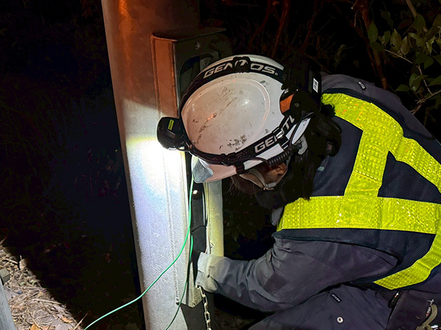 夜間の現場にて、ヘッドライトで手元を照らしながら支柱内の配線作業に集中する作業員のクローズアップ。